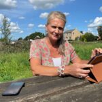 Mirjam aan tafel in park met laptop en telefoon. Achtergrond groen en IJsseldijk