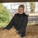 Mirjam in zwarte winterjas pakt een hooibaal op