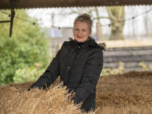 Mirjam in zwarte winterjas pakt een hooibaal op
