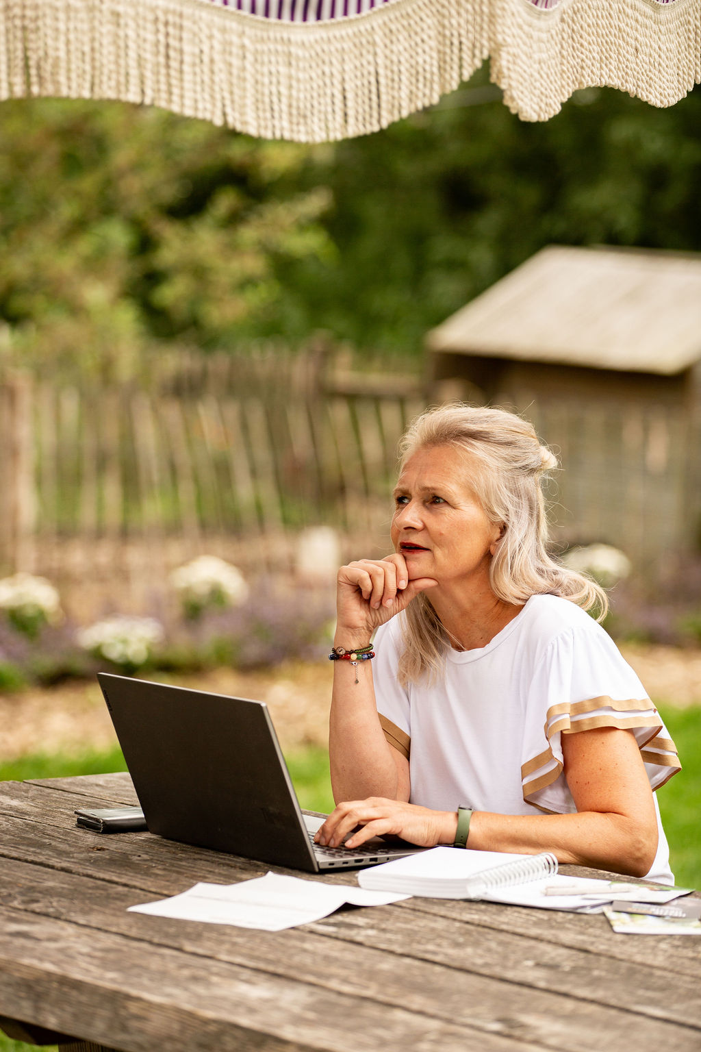 Mirjam werkt achter laptop in tuin van boerderij. Ze denkt na en kijkt voor zich uit.